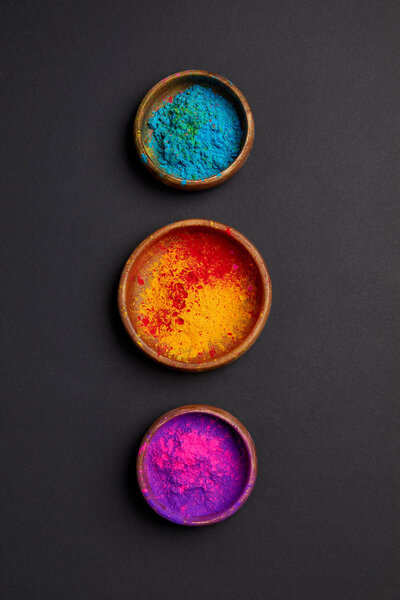 top view of colorful holi powder in bowls in row on grey surface 