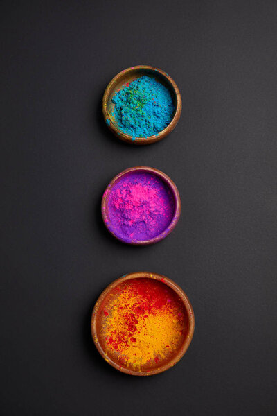 top view of colorful holi paint in bowls in row on grey surface 