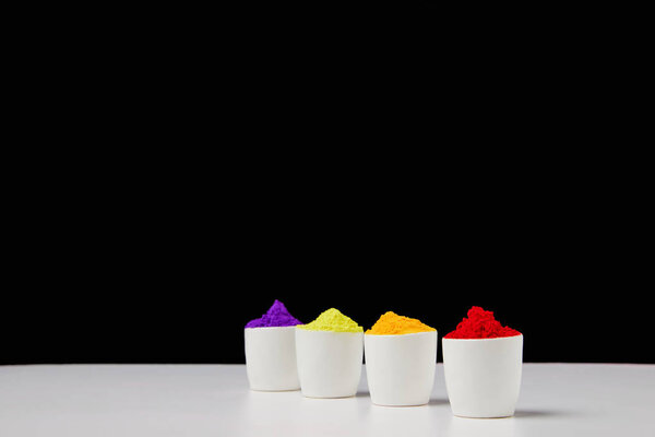 row of colorful holi paint in bowls on black, Hindu spring festival