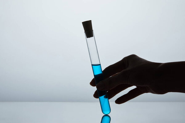 cropped shot of woman holding test tube filled with blue liquid