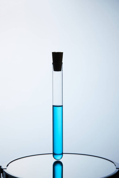 test tube filled with blue liquid standing on reflective surface