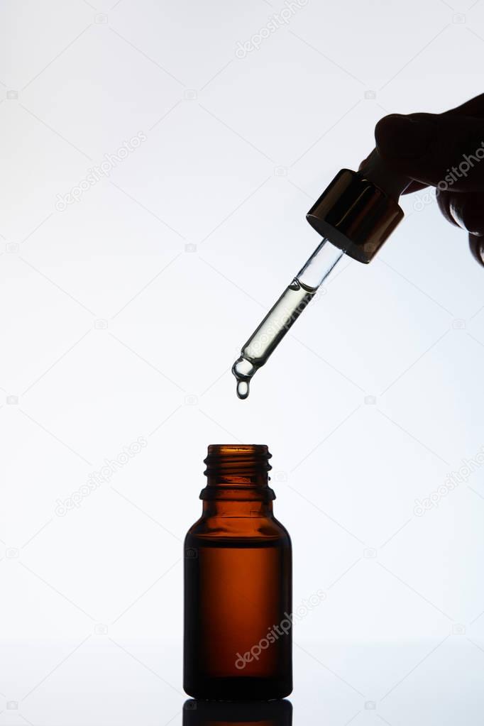 cropped shot of woman dropping oil into bottle from pipette on white