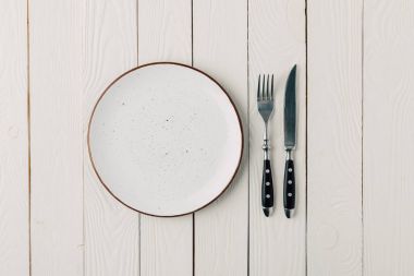 Empty plate and cutlery on white wooden background