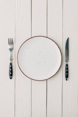 Top view of plate and cutlery on white wooden background clipart