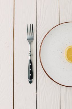 Half of juicy lemon on plate with fork on white wooden background clipart