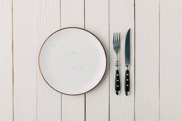 Пустая тарелка и столовые приборы на белом деревянном фоне
