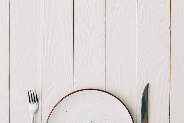 Empty plate with fork and knife on white wooden background