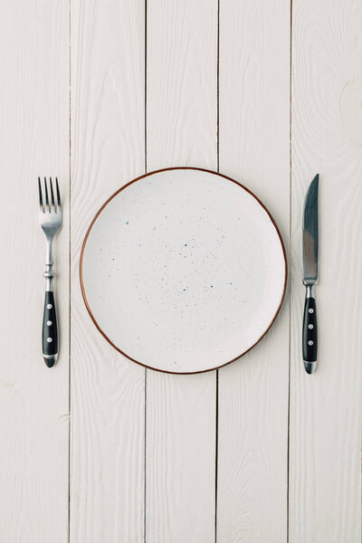 Top view of plate and cutlery on white wooden background