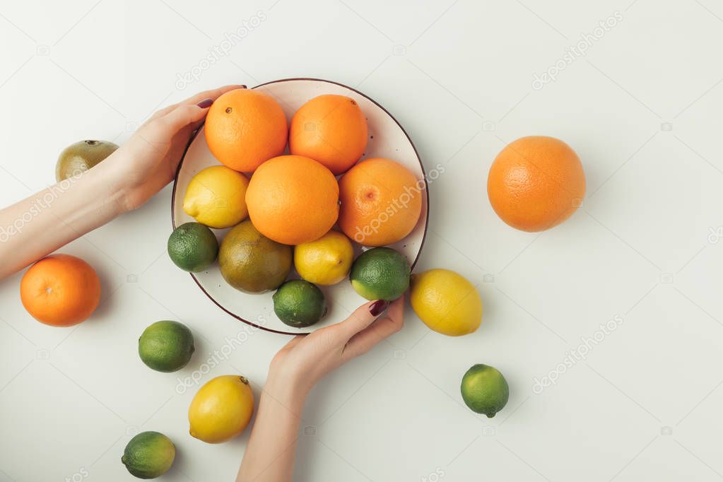 Female hands holding plate with citruses isolated on white background