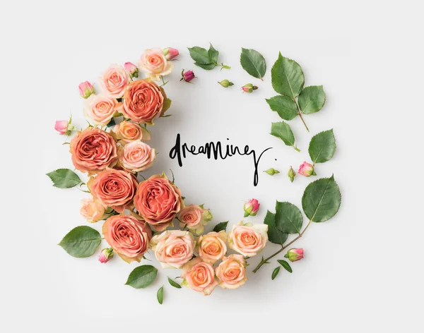 DREAMING sign inside pink flower wreath with leaves, buds and petals isolated on white