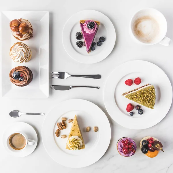 在盘子上排列各种蛋糕的顶端视图 杯咖啡和白色的纸杯蛋糕 — 图库照片