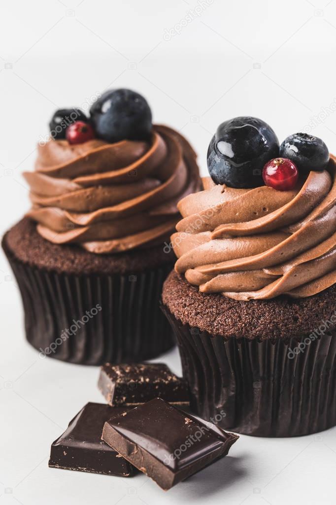 close up view of chocolate cupcakes with cream, grape, berries and pieces of chocolate isolated on white