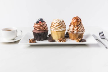 close up view of various cupcakes on plate, cup of coffee and cutlery isolated on white clipart