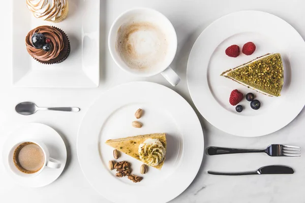top view of arrangement of pieces of various cakes on plates, cups of coffee and cupcakes isolated on white