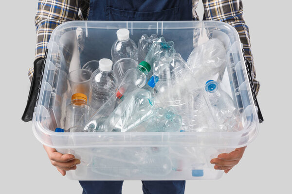 partial view of man holding container with plastic bottles in hands isolated on grey, recycling concept