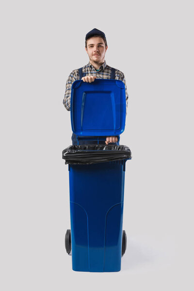 portrait of young cleaner in uniform with trash bin isolated on grey