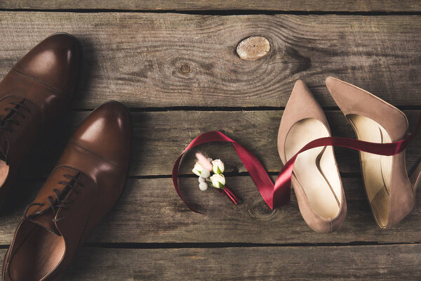 flat lay with ribbon, corsage, bridal and grooms shoes on wooden tabletop
