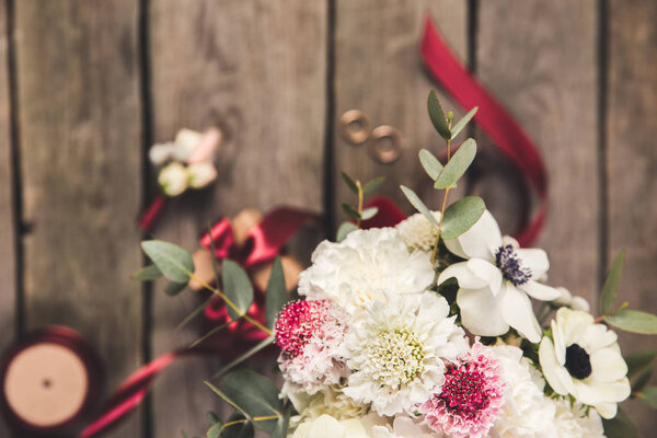 selective focus of beautiful bridal bouquet, wedding rings and ribbons on wooden surface