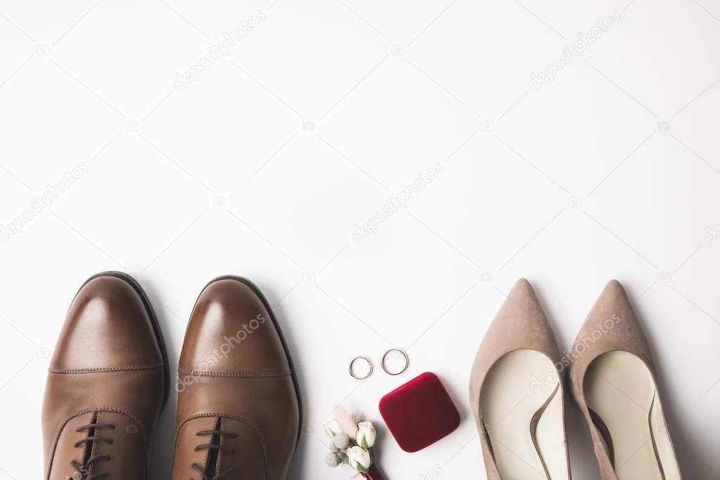 top view of pairs of bridal and grooms shoes, corsage, jewelry box and wedding rings isolated on white