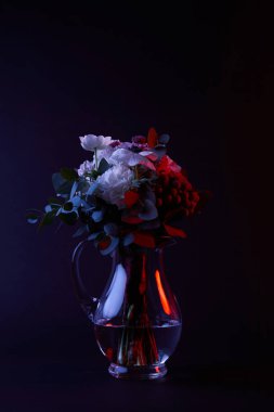 bouquet of different flowers in reflecting glass vase on dark clipart
