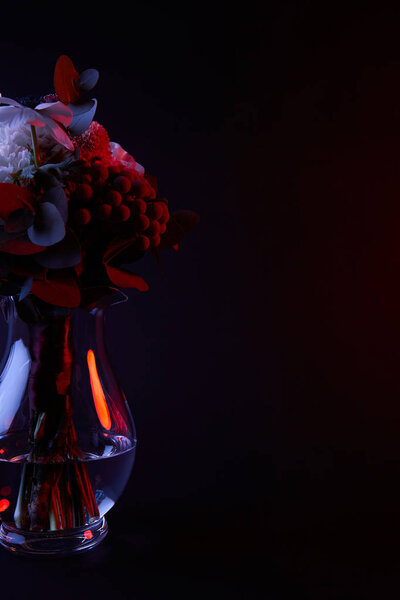 bouquet of different flowers in glass vase with red light on dark