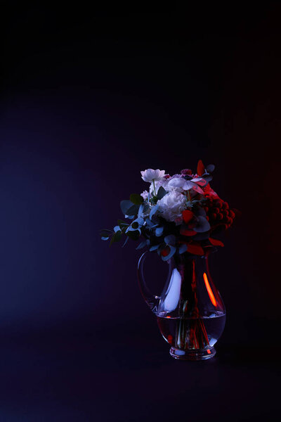 bouquet of different flowers in glass carafe with water on dark
