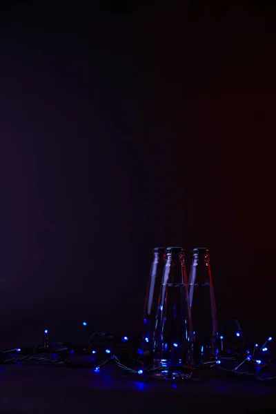 Trei Sticle Închise Apă Ghirlande Albastre Suprafața Întunecată — Fotografie de stoc gratuită