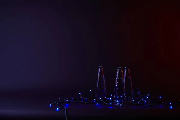 Três Garrafas Água Com Guirlanda Azul Brilhante Superfície Escura — Fotografia de Stock