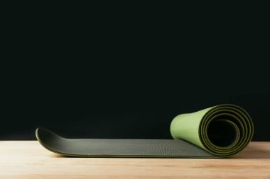 green rolled yoga mat on wooden table on black clipart