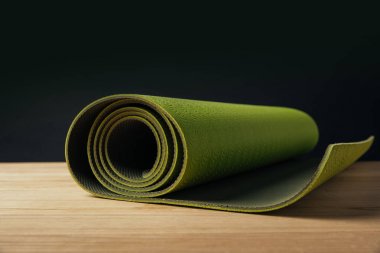 green rolled yoga mat on wooden surface on black clipart