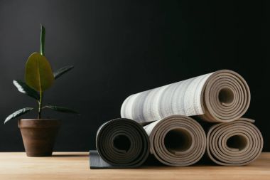 different rolled yoga mats and potted plant on wooden table clipart