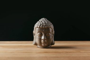 Sculpture of buddha head on wooden tabletop clipart