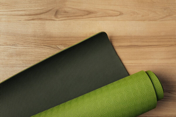 top view of green rolled yoga mat on wooden floor