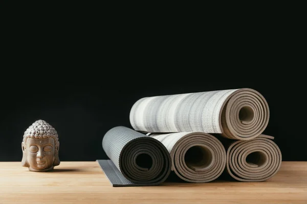不同的滚动瑜伽垫和佛像雕塑在木桌上 — 图库照片