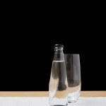 Botella con agua y vaso vacío sobre mesa sobre fondo negro