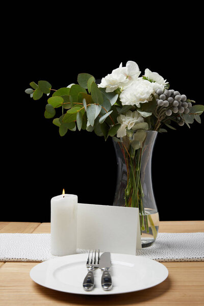 Цветы в вазе со столовыми приборами и тарелками на столе рядом с пустой картой на черном фоне
