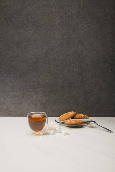 glass cup with fresh hot tea and tasty oatmeal cookies on grey