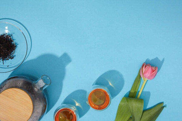 top view of fresh hot tea in cups and teapot and beautiful tulip flower on blue