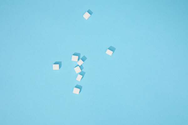 top view of sweet white tasty sugar cubes with shadows on blue