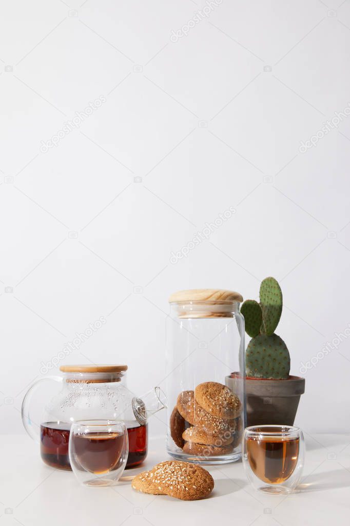 tea in glass cups, tasty cookies, teapot and cactus in pot on grey