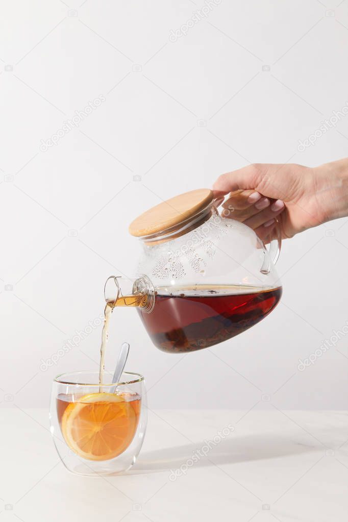 cropped shot of person pouring tea from teapot in cup on grey