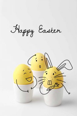 three yellow painted easter eggs in egg stands with comic drawn faces on white clipart