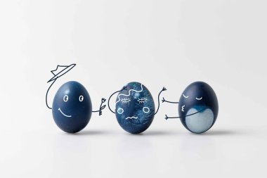 three blue painted easter eggs with comic drawn faces on white surface clipart