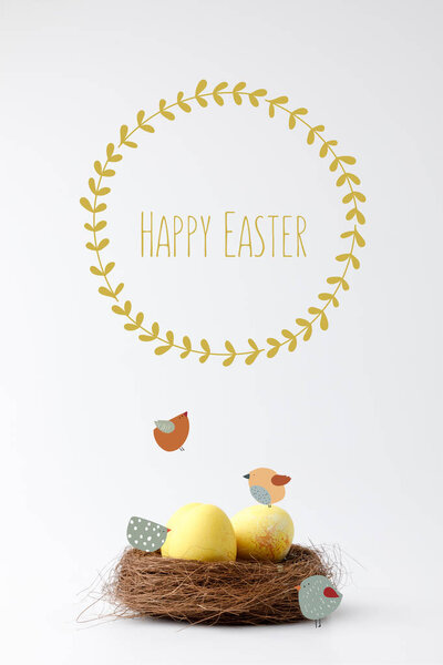 yellow painted easter eggs in decorative nest with drawn birds and happy easter lettering on white