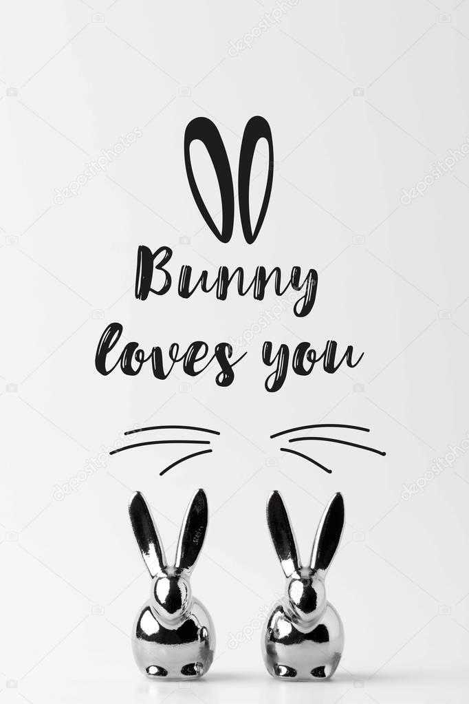 two statuettes of easter bunnies with bunny loves you lettering on white