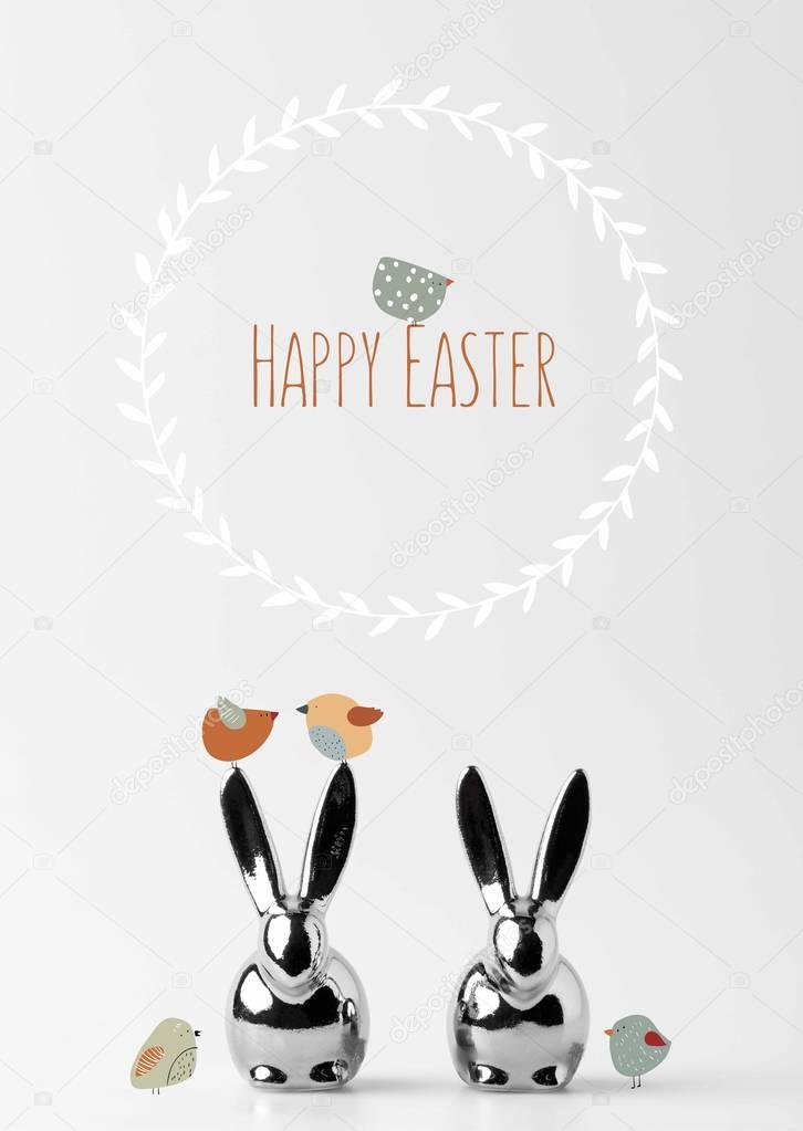 two statuettes of easter bunnies with drawn birds and happy easter lettering on white