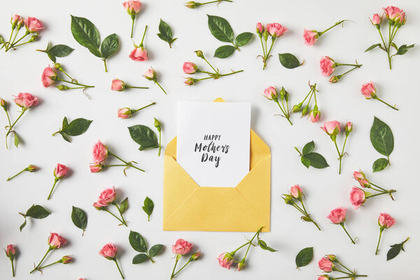 happy mothers day greeting card in envelope and beautiful pink roses and green leaves on grey  