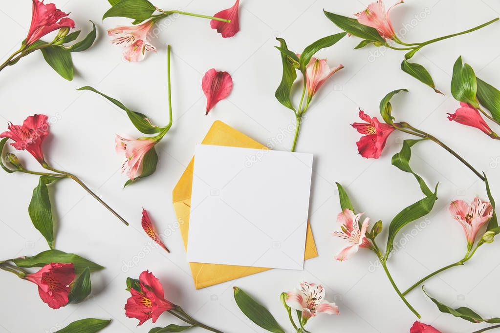 top view of blank card with envelope and beautiful pink flowers with green leaves on grey