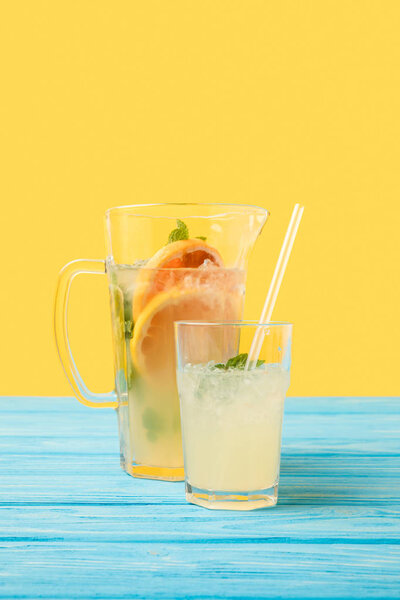 Крупный план свежего холодного летнего напитка в стакане и кувшине на желтом
