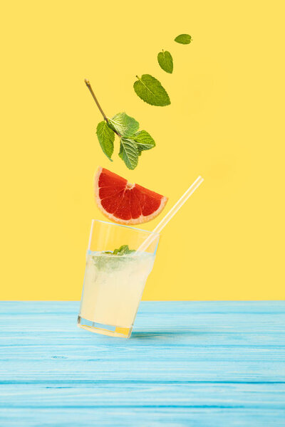 ингредиенты, падающие в стакан со свежим холодным летним коктейлем на желтый
